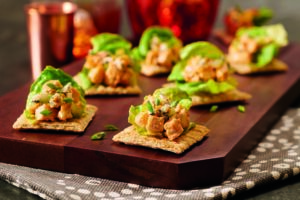 Trisuit crackers topped with chicken and lettuce sitting on top of a dark wooden cutting board